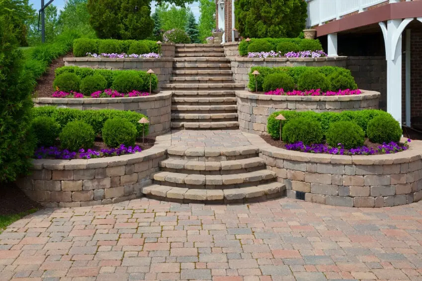 This outdoor garden shows an awesome display of clipped hedges, both square-shaped and round, accompanied by colorful perennial flowers in front, and landscaped to show uniformity of theme per row The elegant architecture of brick stairway and pavement only serves to accentuate the landscaped garden