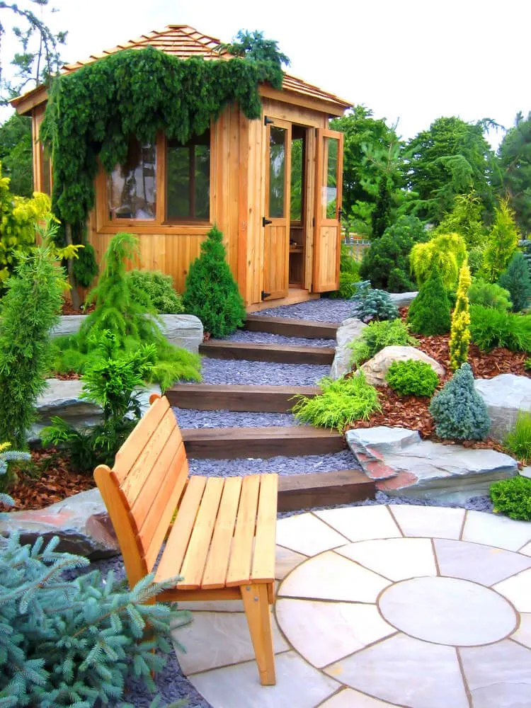 A pebbled pathway separated by layers of wooden steps that’s lined with landscaped shrubs on the sides will lead you from the isolated wooden bench at the paved concrete flagstone to the inviting doors of the wooden gazebo at the top