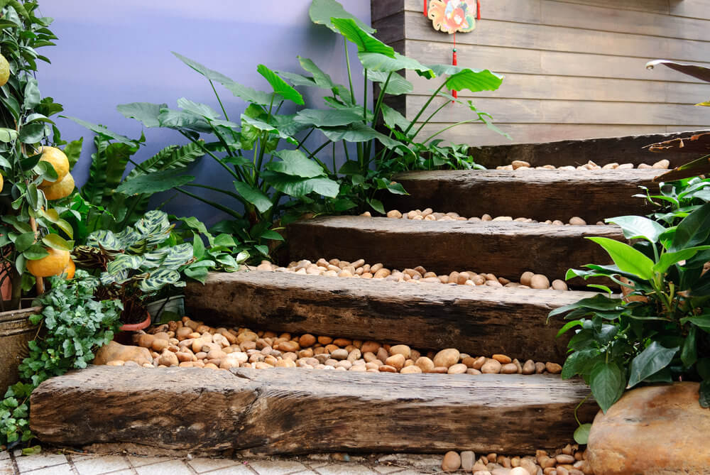 The oriental feel of these garden steps is thanks to the combination of the wood planks loaded with pebbles in between Broad-sized green leaves and a lemon plant, complete with its fruits, serve as ornaments to this neutral-colored environment