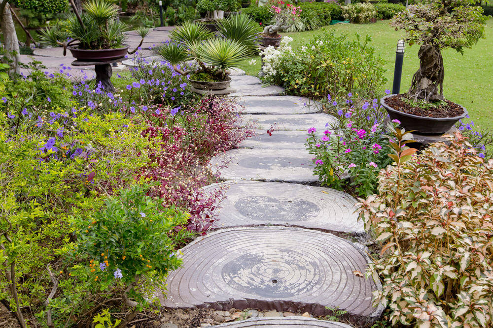 Slices of wood slabs attract a lot of attention as this garden’s pathway is surrounded by flowering plants and low-lying shrubs